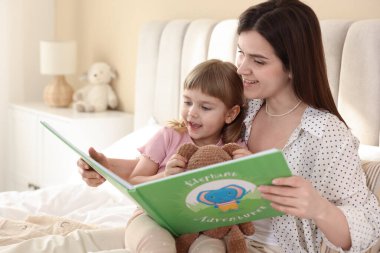Yatma vakti. Mutlu küçük kız, annesiyle evde kitap okuyor.