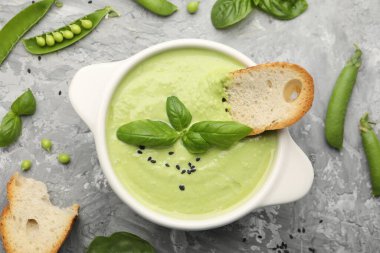 Lezzetli bezelye kremalı çorba fesleğen ve kızarmış ekmek gri masada servis edilir.