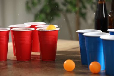 Bira pong oyunu. İçkili plastik bardaklar ve toplar ahşap masada, yakın plan.