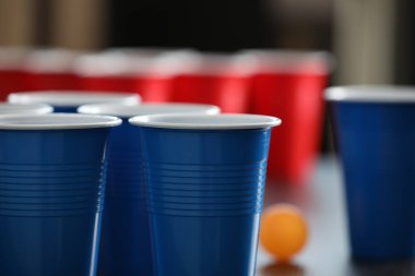 Bira pong oyunu. İçkili plastik bardaklar ve tahta masada top, yakın plan.