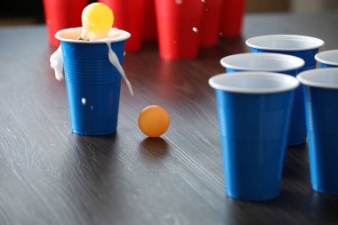 Bira pong oyunu. İçkili plastik bardaklar ve toplar ahşap masada, yakın plan.
