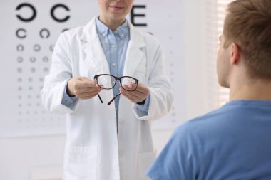 Oftalmolog klinikteki hastaya gözlük veriyor, yakın plan.