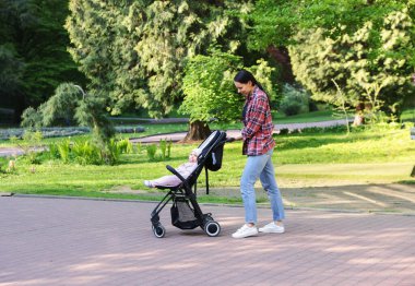 Anne bebeğiyle parkta bebek arabasında yürüyor.