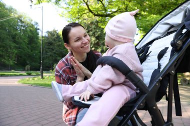 Anne parkta bebek arabasında sevimli bebeğiyle oynuyor.