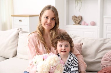 Küçük çocuk evdeki kanepede annesine güzel şakayık çiçekleri veriyor.