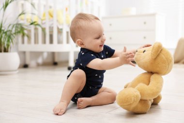 Küçük şirin bebek odada oyuncak ayıyla oynuyor.