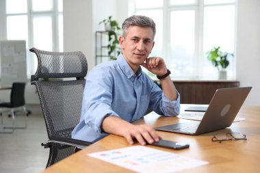 Ofiste dizüstü bilgisayar ve akıllı telefonla çalışan bir iş adamı.