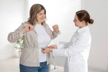 Kilo kaybı. Beslenme uzmanı klinikte kilolu kadının belini bantla ölçüyor.