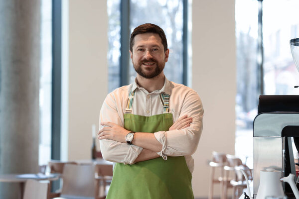 Portrait of smiling business owner with crossed arms in his cafe