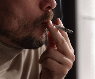 Pencerenin yanında sigara içen adam, yakın plan.