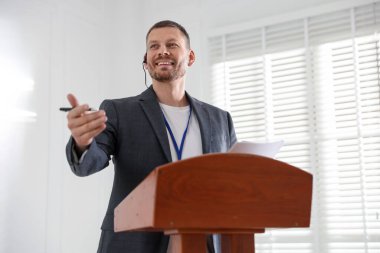 İçerideki kürsüde mikrofonla halka açık konuşma yapan adam.