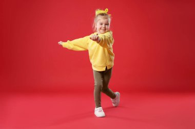 Kırmızı arka planda dans eden tatlı küçük kız.