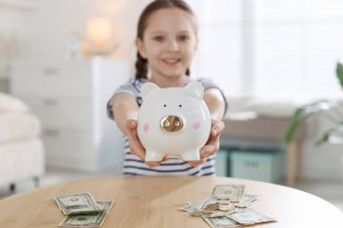 İçerideki masada kumbarası ve cep harçlığı olan kız, seçici odaklı.