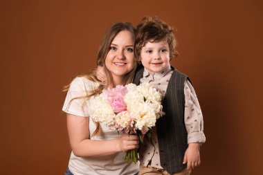 Küçük çocuk kahverengi arka planda annesine güzel şakayık çiçekleri veriyor.