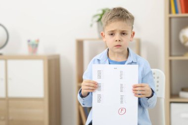 Okul derecesi. Cevap kağıdını tutan üzgün çocuk. Kapalı alanda F harfi, mesaj için boşluk.