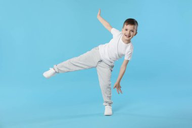 Mutlu küçük çocuk açık mavi arka planda dans ediyor