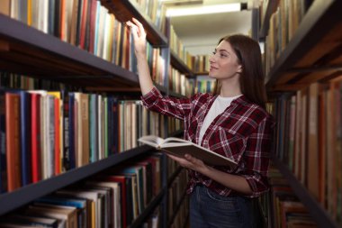Halk kütüphanesinde rafların yanında kitabı olan bir kadın.