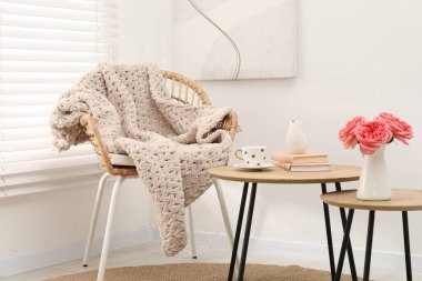 Yünlü battaniyeli hasır sandalye, kitaplar, vazodaki güzel çiçekler ve kapalı masalardaki fincanlar.