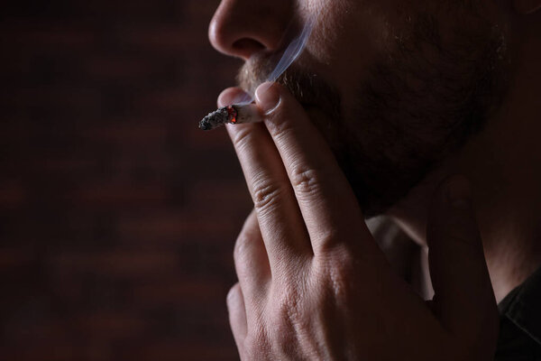 Man smoking cigarette on blurred background, closeup. Space for text