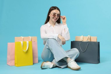 Açık mavi arka planda alışveriş torbaları olan pozitif kadın.
