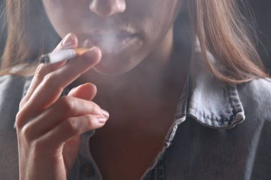 Arka planda sigara içen tişörtlü bir kadın, yakın plan. Kötü alışkanlık.