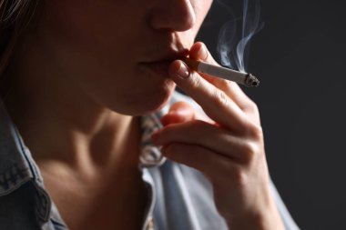 Arka planda sigara içen tişörtlü bir kadın, yakın plan. Kötü alışkanlık.