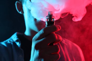Karanlık arka planda neon lambalarda elektronik sigara içen adam, yakın plan