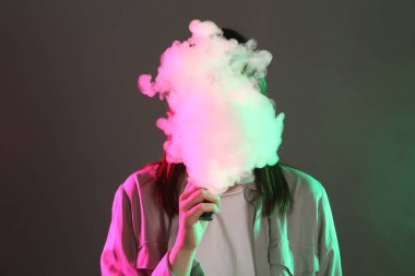 Gri arkaplandaki neon ışıklarda elektronik sigara içen kadın