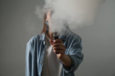 Gri arka planda elektronik sigara içen kadın