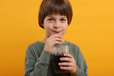 Tatlı küçük çocuk turuncu arka planda ferahlatıcı soda içiyor.