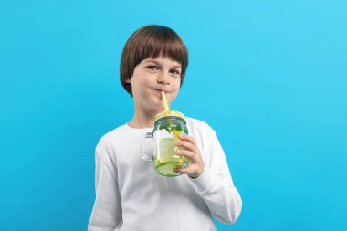 Açık mavi arka planda limonata içen şirin bir çocuk. Tazeleyici içecek.