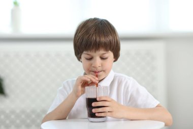Şirin küçük çocuk, kapalı bir masada ferahlatıcı soda içiyor.