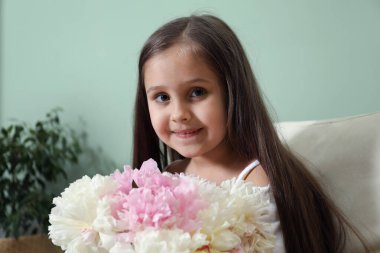 Güzel şakayık demeti olan şirin küçük kız yeşil duvarın yanındaki koltukta.