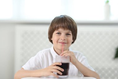 Şirin küçük çocuk, kapalı bir masada ferahlatıcı soda içiyor.
