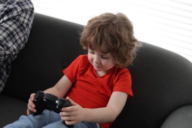 Küçük çocuk ve babası evde oyun kontrolörüyle oynuyorlar.