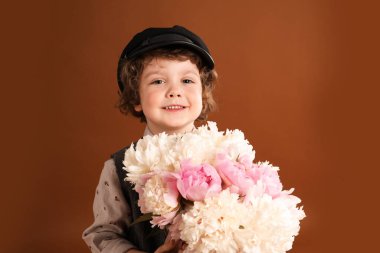 Kahverengi arka planda bir buket güzel şakayığı olan sevimli küçük bir çocuk.