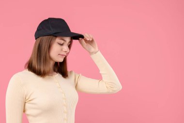 Pembe arka planda siyah beysbol şapkası takan genç bir kadın.