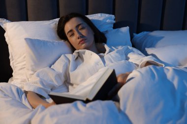 Evde kitapla uyuyan genç bir kadın.