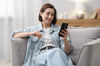 Evdeki koltukta modern akıllı telefon kullanan bir kadın.