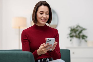 Evdeki koltukta modern akıllı telefon kullanan bir kadın.