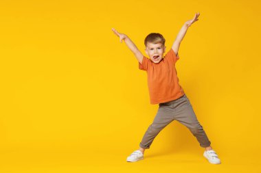 Mutlu küçük çocuk turuncu arka planda dans ediyor, mesaj için yer var.