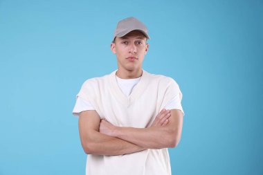 Genç adam açık mavi arka planda şık gri beyzbol şapkası giyiyor.