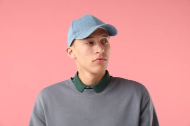 Pembe arka planda şık bir beyzbol şapkası takan genç adam.