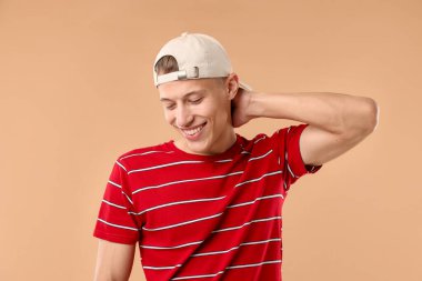 Beyzbol şapkalı genç adam bej arka planda.