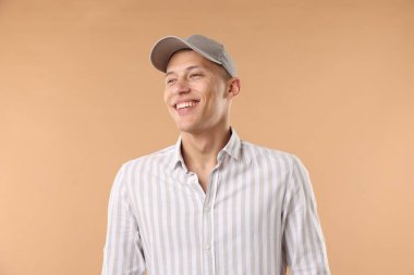 Beyzbol şapkalı genç adam bej arka planda.