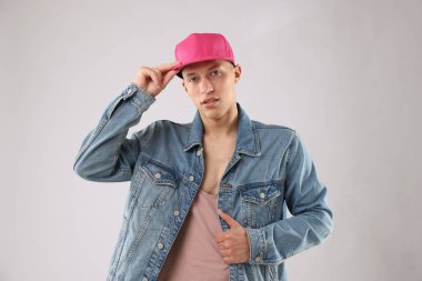 Açık gri arka planda şık bir beyzbol şapkası takan genç adam.