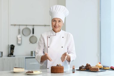 Gülümseyen pasta şefi mutfaktaki tatlılarla masada.