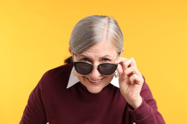 Turuncu arka planda şık giyinmiş mutlu bir son sınıf kadını.