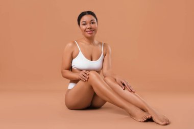 Beyaz iç çamaşırlı, pürüzsüz bir kadın. Bej arka planda epilasyon işleminden sonra.