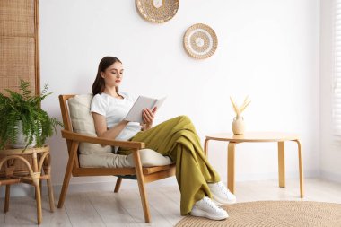 Evdeki rahat koltukta kitap okuyan güzel bir kadın.